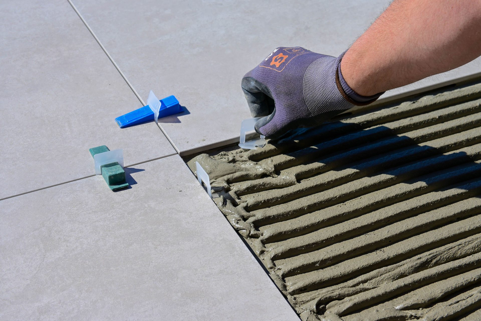 A gloved hand setting spacers on a pale tiled floor.